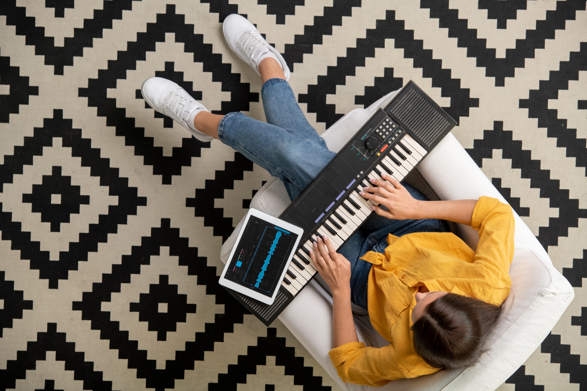Overview of young female using synthesizer keyboard while recording music